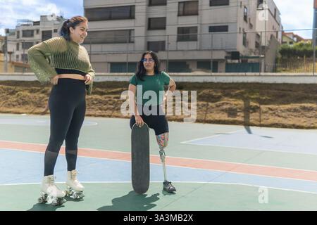 Zwei Freunde, einer mit einer Beinprothese und Skateboard und der andere mit Rollschuhen, genießen einen sonnigen Tag im Skatepark Stockfoto