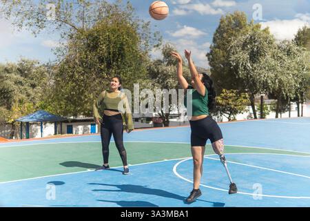 Zwei Freunde spielen Basketball auf dem Platz im Freien, einer mit Beinprothesen und genießen den sonnigen Tag Stockfoto