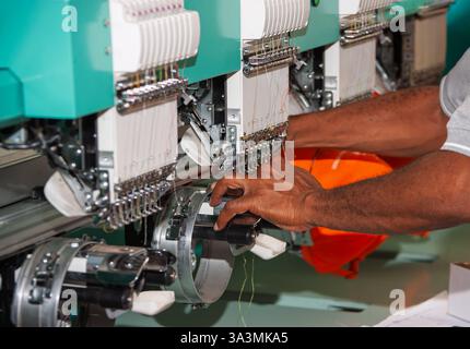 Stickmaschine mehrköpfiger Industriearbeiter, afroamerikanischer Arbeiter in einer Bekleidungs-Textilfabrik Stockfoto
