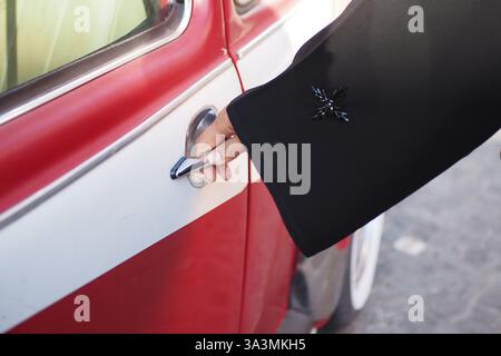 Die Hand greift mittags nach der Autotür in einem roten Vintage-Fahrzeug Stockfoto