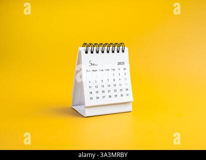 Ein Schreibtischkalender für Mai 2025 für Organisatoren, die stehen, isoliert auf gelbem horizontalen Hintergrund, minimalistisch. Weißer kleiner Tischkalender Stockfoto