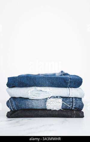 Jeansstapel aus Denim in verschiedenen Farben, ordentlich gefaltet und auf minimalistischem Hintergrund gestapelt Stockfoto
