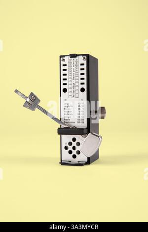 Klassisches analoges schwarzes und metallisches Metronom, isoliert auf gelbem Hintergrund. Stockfoto