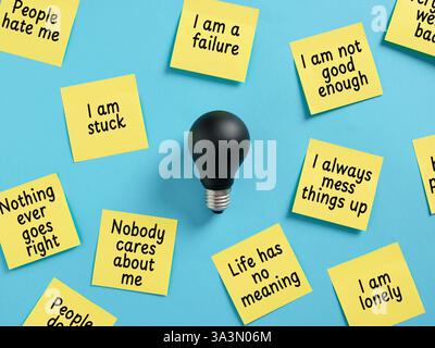 Schwarze Glühbirne auf einer blauen Oberfläche, umgeben von gelben Haftnotizen voller negativer Gedanken und Mindset. Stockfoto