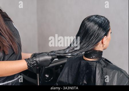 Haarpflege für Kunden, Friseur, der pflegende Maske auf das Haar des Mädchens im Schönheitssalon aufträgt. Stockfoto
