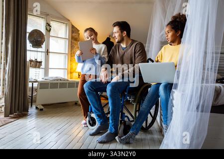 Glücklicher Vater im Rollstuhl mit interrassischen Töchtern mit Laptop zusammen, Bildung, lustiges Konzept Stockfoto