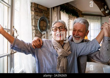 Glückliche reife Frau, die mit ihrem älteren Mann zu Hause tanzt, aktives gesundes Seniorenpaar Stockfoto