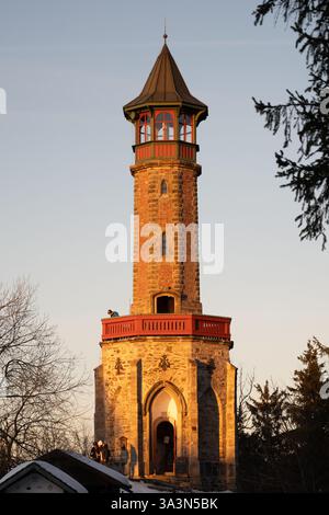 Der Stepanka Aussichtsturm steht an einem Winterabend im Isergebirge hoch. Der warme Glanz des Sonnenuntergangs unterstreicht die Architektur vor einem kühlen Hintergrund. Stockfoto