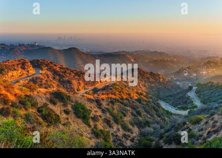 Gewundene Wanderwege im Griffith Park, atemberaubender Blick auf das Griffith Observatory und die trübe Skyline der Innenstadt von Los Angeles in der Ferne während der goldenen Stunde. Stockfoto