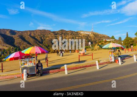 Los Angeles, Kalifornien - 20. Dezember 2024: Farbenfrohe Imbissstände säumen die Straße vor dem Hollywood-Schild, umgeben von Besuchern, die einen sonnenuntergang genießen Stockfoto
