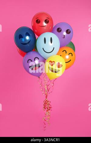 Gesichter mit verschiedenen Emotionen auf hellen Ballons vor rosa Hintergrund Stockfoto