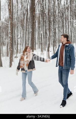 Ein fröhliches Paar schlendert Hand in Hand durch einen verschneiten Wald und fängt im Winter die Liebe ein Stockfoto