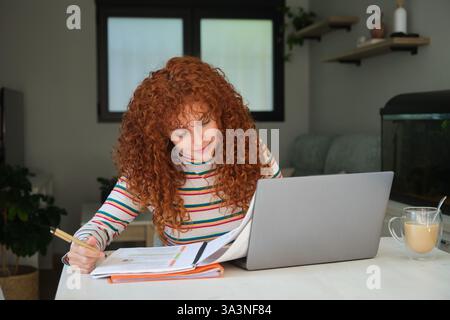 Junge Frau, die zu Hause mit Laptop studiert und Notizen macht Stockfoto