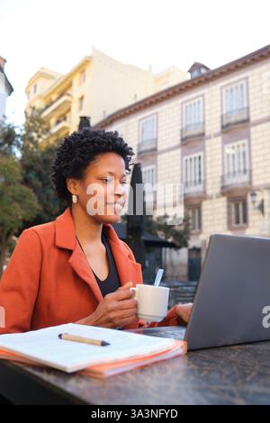 Frau, die mit Laptop arbeitet und draußen in Madrid Kaffee trinkt Stockfoto