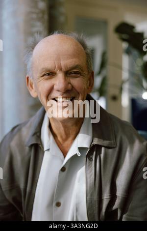 Nahaufnahme eines älteren Mannes, der in Innenräumen mit natürlichem Licht warm lächelt. Stockfoto