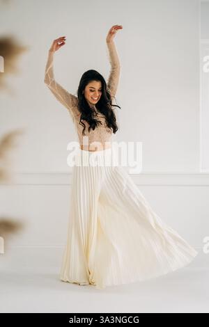 Frau, die sich fröhlich in einem Plissee-Rock und einem transparenten Oberteil dreht, Arme angehoben Stockfoto