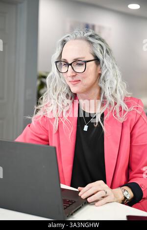 Professionelle Frau in rosa Blazer konzentriert sich auf einen Laptop in einem Werk Stockfoto