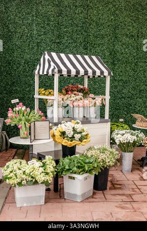 Blumenwagen mit lebhaften Blumensträußen unter gestreiftem Baldachin im Freien. Stockfoto