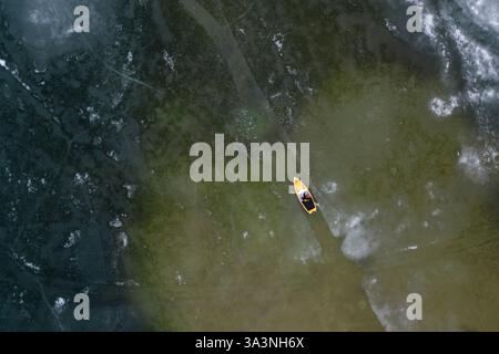 Gelbes Paddleboard, das durch eisiges Wasser auf einem Wintersee schneidet Stockfoto