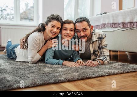 Mutter, Vater und Sohn genießen die Freundschaftszeit auf einem gemütlichen Teppich auf dem Boden des Mädchens. Hochwertiger Familienmoment Stockfoto