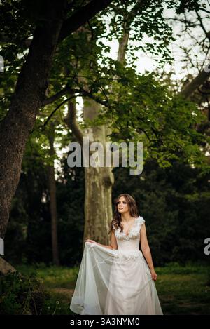 Atemberaubende Braut posiert anmutig in einem Frühlingspark, inmitten blühender Bäume. Strahlt Eleganz aus, Stockfoto