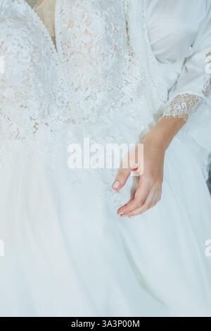 Ein detailliertes Nahaufnahme-Foto einer eleganten Hand einer Frau, die anmutig auf einem wunderschönen weißen Kleid ruht, das das Auge auffällt Stockfoto