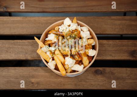 Poutine-Pommes mit Käse und Soße in Papierbehälter zum Mitnehmen. Köstliche, frisch zubereitete Mahlzeit, perfekt für Menüs, Restaurants oder Speisen Stockfoto