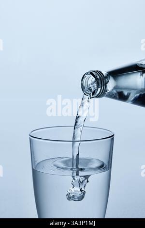 Nahaufnahme des Wassers, das aus der Glasflasche in klares Glas gegossen wird, mit Blasen und fließendem Strom vor hellblauem Hintergrund. Mock-Up. Stockfoto