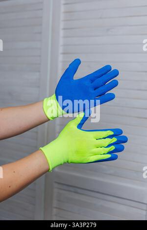 Eine Person trägt ein leuchtendes Paar neongelber und blauer Handschuhe, die für verschiedene Aufgaben, insbesondere Haushaltsreinigungsaufgaben, entwickelt wurden Stockfoto