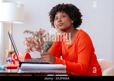 Nachdenkliche Afroamerikanerin, die zu Hause mit Laptop und Notebook studiert Stockfoto
