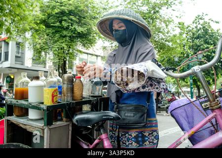 Straßenverkäufer, der Kräutermedizin auf ihrem Fahrrad in yogyakarta zubereitete, trug traditionellen Hut und Gesichtsmaske Stockfoto