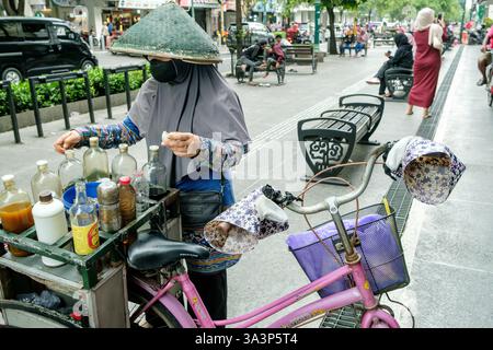 Javanische Frau mit konischem Hut und Gesichtsmaske, die traditionelle Kräutermedizin von ihrem Fahrradwagen in yogyakarta, indonesien, verkauft Stockfoto