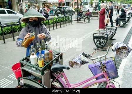 Javanische Frau mit konischem Hut und Gesichtsmaske, die jamu Kräutermedizin auf der malioboro Straße in yogyakarta, indonesien, ausgießt Stockfoto