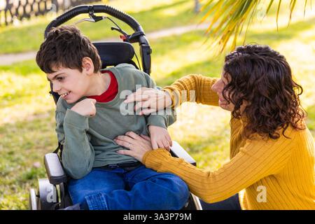 Mutter spielt mit behindertem Sohn im Rollstuhl im Park Stockfoto