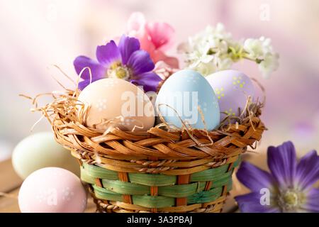 Ostereier und Blumen in einem Korb draußen auf Holztisch mit farbenfrohem Frühlingshintergrund Stockfoto