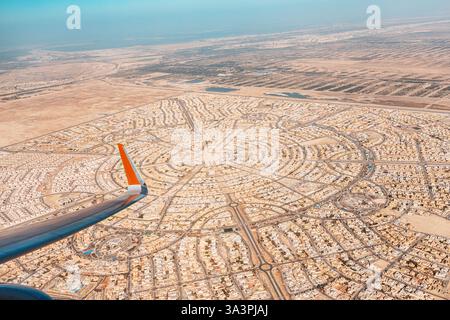 Flügel eines Flugzeugs, das über eine kreisförmige Wüstenstadt in Abu Dhabi fliegt, zeigt Stadtentwicklung und Infrastruktur Stockfoto