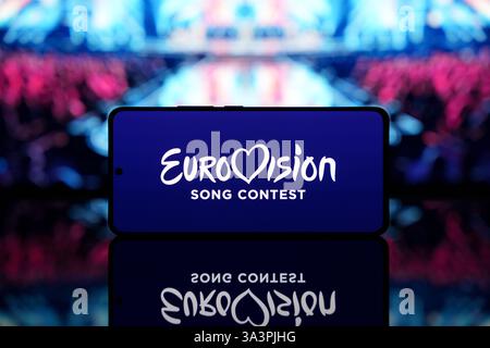 Smartphone mit Eurovision Song Contest Logo mit verschwommener Bühne und Publikum im Hintergrund. Musikwettbewerb und Unterhaltungskonzept Stockfoto