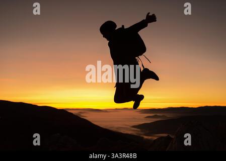 Ein glücklicher, fröhlicher Mann, der auf einen Berg springt, mit ausgestreckten Armen Konzept des Erfolgs der freien Freiheit, des aktiven Lebensstils Stockfoto