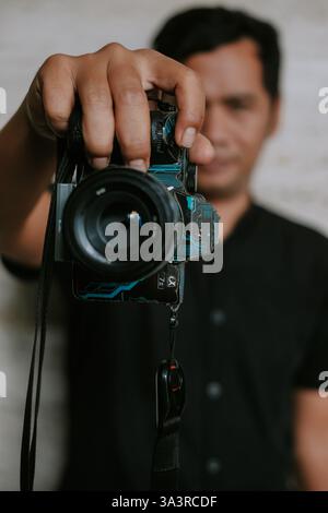 Porträt eines Mannes, der eine Digitalkamera in der Hand hält und sich auf die Aufnahme des Moments konzentriert. Die Kamera verfügt über ein maßgeschneidertes Schaltungsdesign, eine Mischung aus Elektronik Stockfoto