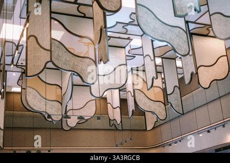 Eine moderne und künstlerische Deckendekoration mit strukturierten Paneelen, die an konturierten Metallrahmen hängen. Diese auffällige Installation kombiniert Geom Stockfoto