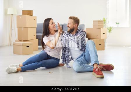 Paare, die sich gegenseitig High 5 geben, sitzen in einer neuen Wohnung mit Hausschlüsseln zwischen Pappschachteln Stockfoto