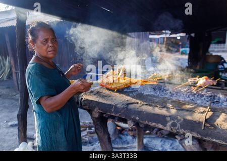 Eine Frau, die Fisch auf einem offenen Feuer auf einem Straßenmarkt in der Nähe von Baucau in der Demokratischen Republik Timor-Leste kocht. Stockfoto