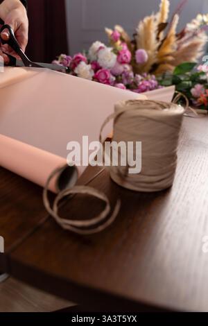 Florist stellt eine Komposition von Blumen aus Rosen und Nelken für den Kunden her. Einpacken eines Blumenstraußes aus gemischten Blumen in Packpapier von Florist in flo Stockfoto