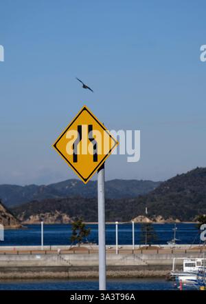 Hawk fliegt über ein gelbes Straßenschild in Naoshima, Japan Stockfoto