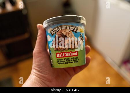 In der gemütlichen Küche hält die verwöhnende Hand eine Wanne Eis mit Brownie-Stücken und Keksteig Stockfoto