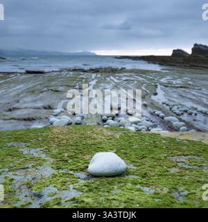 Eine felsige Küste im Norden Spaniens mit glatten Steinen, grünen Moosflecken und Gezeitenbecken. Stockfoto