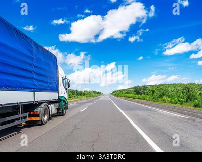 Ein großer Lastwagen mit blauem Planenanhänger fährt auf einer geraden Autobahn Stockfoto