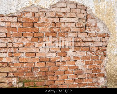 Alte verwitterte Ziegelmauer mit zerbröckelndem Putz, teilweise freigelegt rote Ziegelsteine, raue Textur, veraltete Konstruktion, historische Architektur, rustikal und W Stockfoto