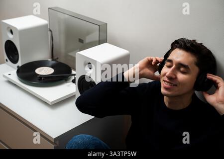 Vinyl-Musikliebhaber. Happy Hipster genießt LP-Aufnahmen mit HiFi-Sound. Ein fröhlicher Musiker mit Kopfhörern hört eine Retro-Schallplatte auf Stockfoto