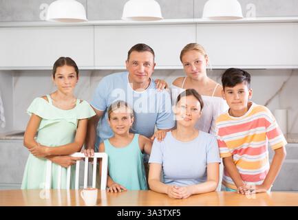 Glücklicher Vater und Mutter mit drei Töchtern und Sohn stehen neben dem Küchentisch. Stockfoto